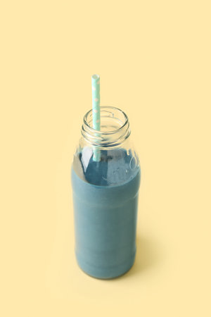 Glass bottle of tasty blue smoothie with straw on yellow backgroundの写真素材