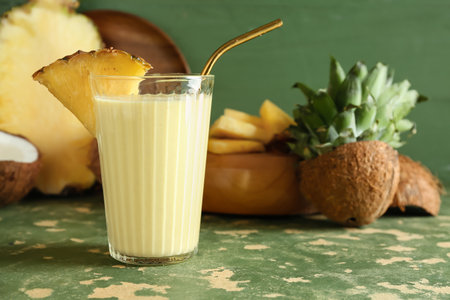 Glass of tasty pineapple smoothie, straw and coconut on green grunge tableの写真素材