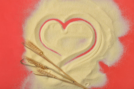 Heart made of raw semolina on red backgroundの写真素材