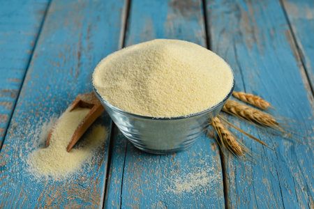 Bowl of raw semolina and spikelets on blue wooden backgroundの写真素材