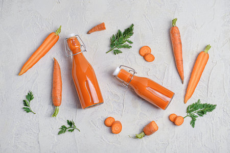 Glass bottles of tasty carrot juice on light grunge backgroundの写真素材