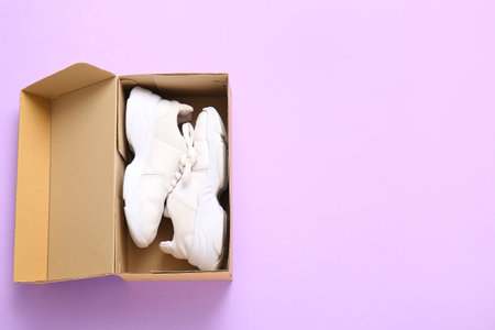 Cardboard box with sports shoes on lilac backgroundの写真素材