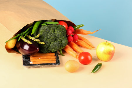 Paper bag with vegetables, fruits and sausages on tableの写真素材