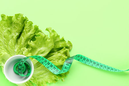 Lettuce and bowl with measuring tape on green background. Diet conceptの写真素材