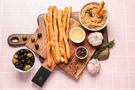 Wooden boards with tasty Italian Grissini and hummus on pink tile backgroundの写真素材