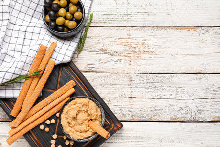 Bowl with tasty hummus and Italian Grissini on light wooden backgroundの写真素材