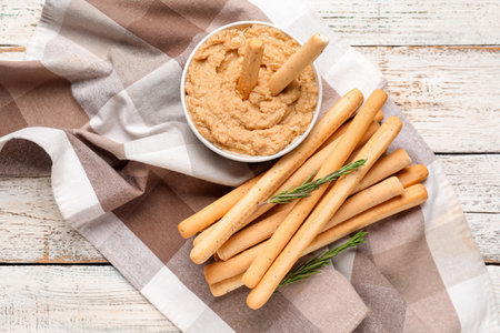 Bowl with tasty hummus and Italian grissini on light wooden backgroundの写真素材