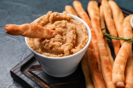 Wooden board with tasty Italian Grissini and hummus on dark background, closeupの写真素材
