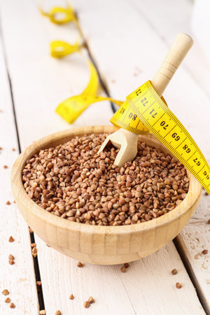 Bowl with buckwheat and yellow measuring tape on light wooden background. Diet conceptの写真素材