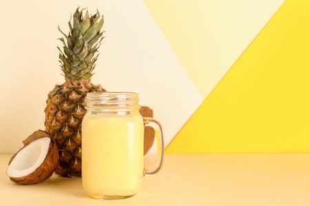 Mason jar of tasty pineapple smoothie and coconut on color backgroundの写真素材