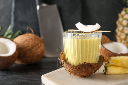 Board with glass of tasty pineapple smoothie and coconut on black grunge table