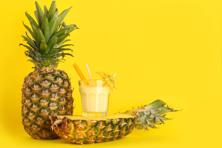 Glass of tasty pineapple smoothie, straw and umbrella on yellow background