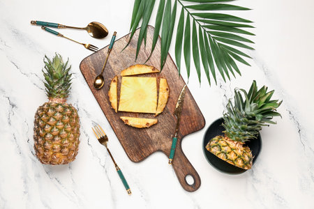 Wooden board with cut pineapple and palm leaf on light backgroundの写真素材
