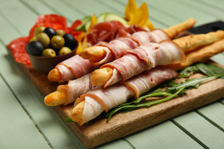 Board of tasty Italian Grissini with bacon on green wooden background, closeupの写真素材
