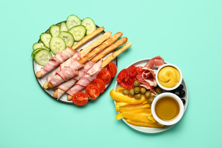 Plates of tasty Italian Grissini with bacon and vegetables on turquoise backgroundの写真素材