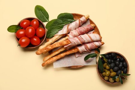 Plate of tasty Italian Grissini with bacon, tomatoes and olives on yellow backgroundの写真素材