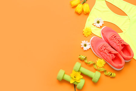 Sportswear with dumbbells and spring flowers on color backgroundの写真素材