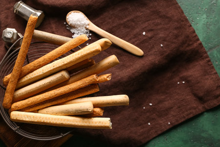 basket with tasty Italian Grissini on green background