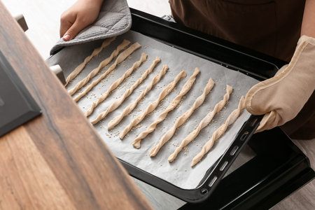Woman putting baking sheet with Italian Grissini into oven, closeup