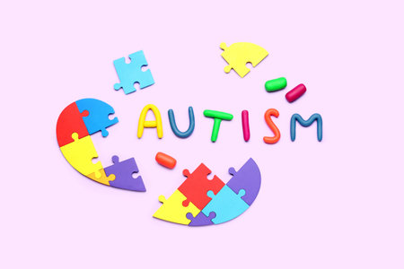 Word AUTISM with puzzle pieces on lilac background