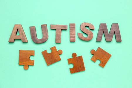 Word AUTISM with puzzle pieces on green background