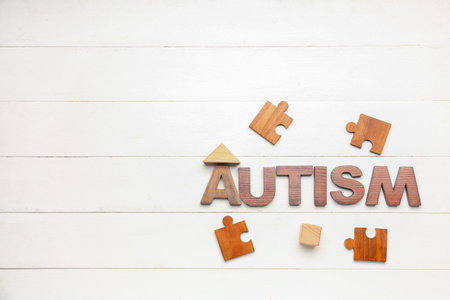 Word AUTISM with puzzle pieces and baby toys on white wooden backgroundの写真素材