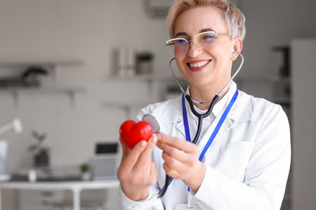 Mature female cardiologist with small red heart and stethoscope in clinicの写真素材