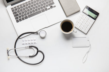 Stethoscope, laptop, coffee, pills and badge on doctor's tableの写真素材