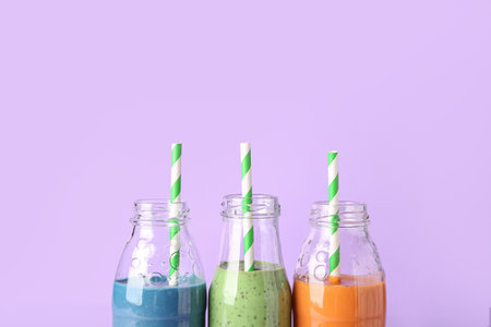 Glass bottles of different tasty smoothie with straws on violet backgroundの写真素材