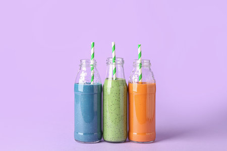 Glass bottles of different tasty smoothie with straws on violet backgroundの写真素材