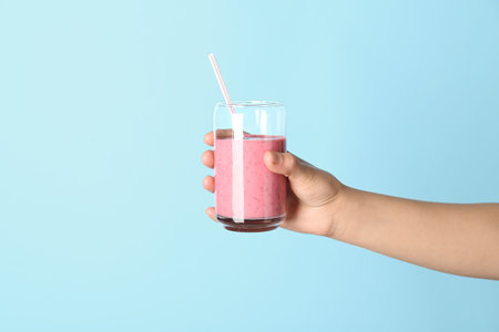 Female hand with glass of pink smoothie on blue backgroundの写真素材