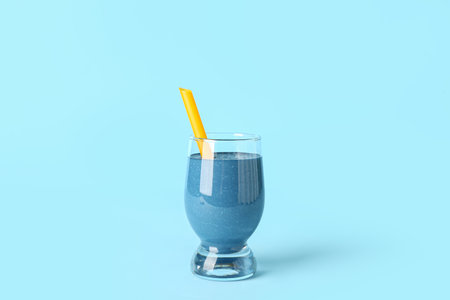 Glass of tasty blue smoothie with straw on color backgroundの写真素材