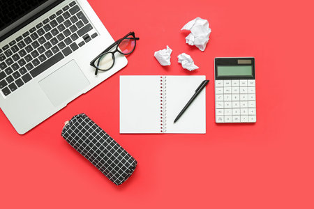 Composition with notepad, calculator, laptop and eyeglasses on red background