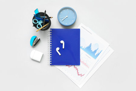 Composition with notepad, clock, stationery and earphones on light background