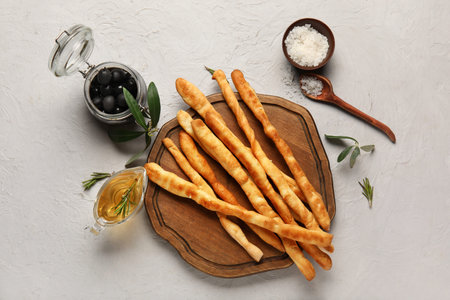 Wooden board with tasty Italian Grissini on light background