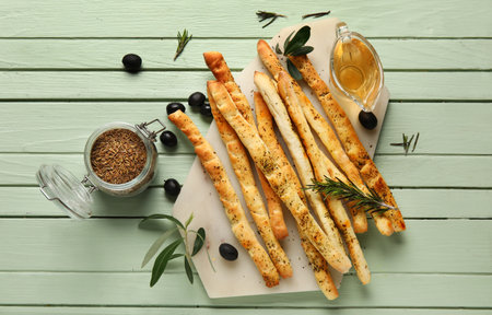 Board of tasty Italian Grissini and jar with thyme on green wooden backgroundの写真素材