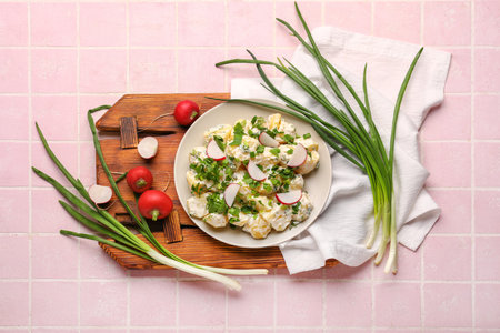 Plate of tasty Potato Salad with greens and radish on pink tile backgroundの写真素材