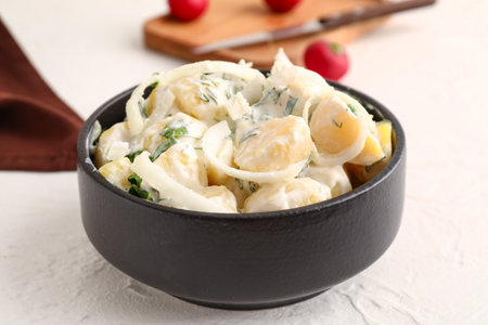 Bowl of tasty Potato Salad with greens and onion on light backgroundの写真素材