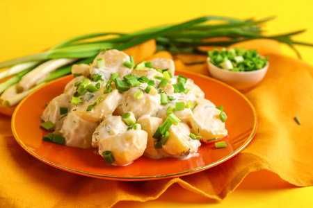 Plate of tasty Potato Salad with greens on yellow backgroundの写真素材