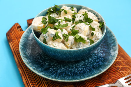Bowl of tasty Potato Salad with greens on blue backgroundの写真素材