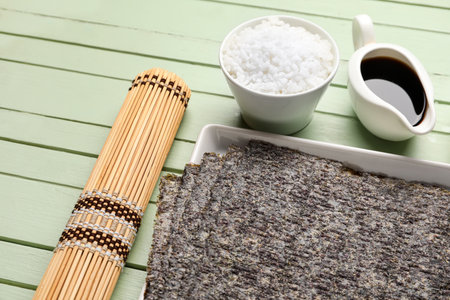 Plate with nori sheets, soy sauce, rice and bamboo mat on color wooden background, closeupの写真素材