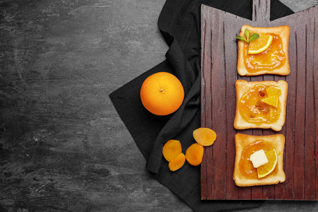 Wooden board of tasty toasts with orange jam on dark backgroundの写真素材
