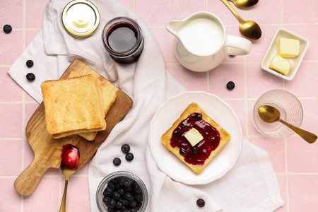 Wooden board with tasty toasts, blueberry jam, jug of milk and berries on pink tile backgroundの写真素材