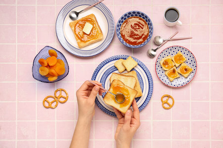 Woman preparing tasty toasts with apricot jam on pink tile backgroundの写真素材