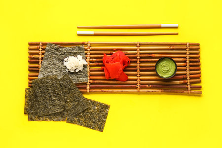 Bamboo mat with nori sheets, rice, ginger and wasabi on yellow backgroundの写真素材