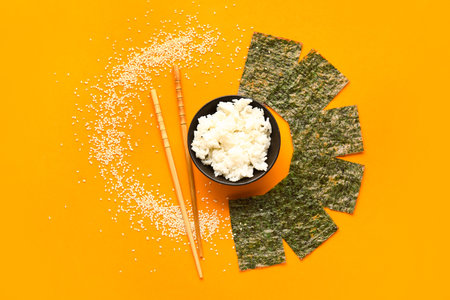 Composition with bowl of rice, nori sheets, sesame seeds and chopsticks on color backgroundの写真素材