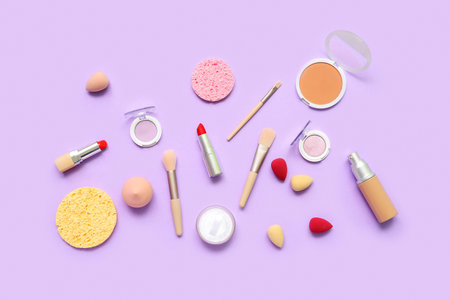 Decorative cosmetics with makeup brushes and sponges on lilac backgroundの写真素材