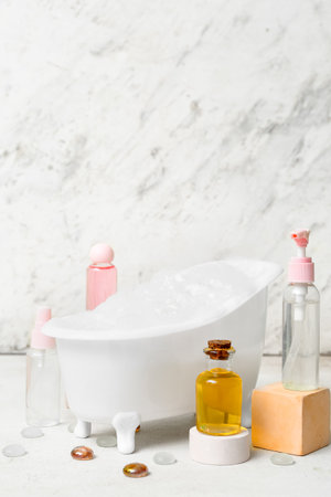 Small bathtub with foam and bottles of cosmetic products on light backgroundの写真素材
