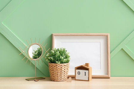 Artificial houseplant with mirror, calendar and blank frame on table near green wallの写真素材