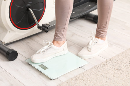 Sporty mature woman measuring her weight on scales at home, closeupの写真素材